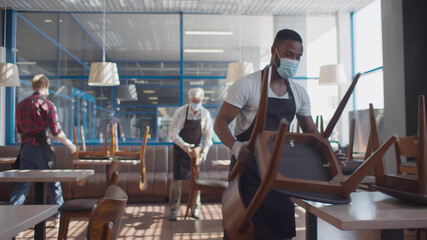 Fototapeta na wymiar Multiethnic staff in facial masks preraing restaurant for reopening after quarantine