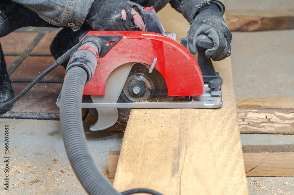 Wall mural Carpenter cuts wooden board with hand-held circular saw