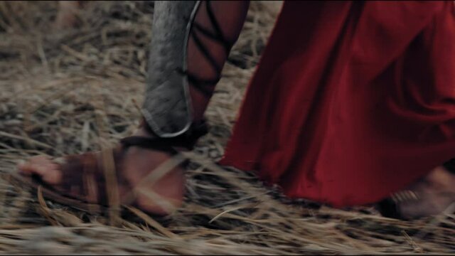 Legs in sandals of spartan walking through dry field.