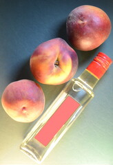 three ripe peaches close-up over a bottle with a pink label on an embossed leathery azure green background, top view