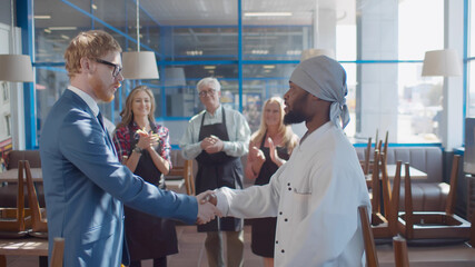 Side view of youmg male manager shaking hands and applauding to new african chef