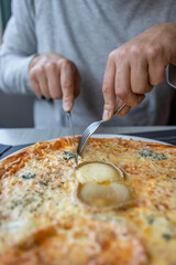 Man hands cut a piece of cheesy pizza in the restaurant