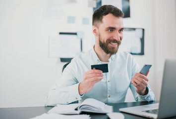 Naklejka na ściany i meble handsome smiling bearded businessman in elegant shirt sits in office showing bank card looking excited while working on business project , money making motivation concept