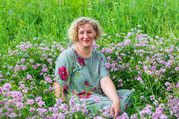 portrait of a young woman sitting in pink flowers on a green lawn on a summer day