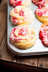 Fresh sweet bun with cream and raspberries on the rustic wooden background. Selective focus. 
