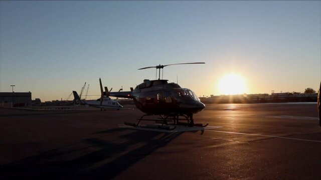 Helicopter parked at a hanger with sun setting and blue sky.