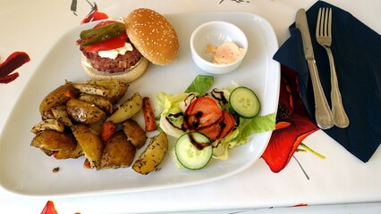 Handmade wild boar burger with cucumber, tomato, mayonnaise and baked potatoes and carrots, salad with balsamic vinegar and spicy sauce