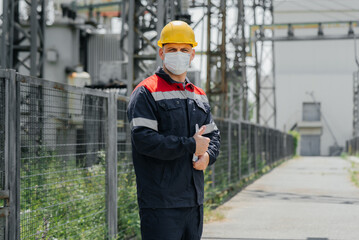 During the pandemic, a masked electrical substation engineer inspects high-voltage equipment. Energy. Industry.