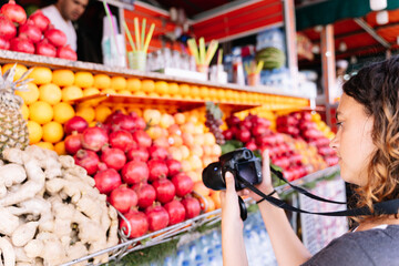 Selective focus on a woman taking a photo with a digital camera in front of a fruit stand