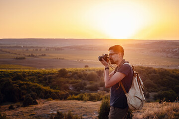 Man photographer with backpack and camera taking photo of sunset mountains