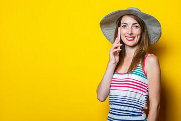 Happy young woman in hat talking on the phone on yellow background.