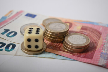 There are a few banknotes and euro coins to be seen. Over it is a cube with a six.