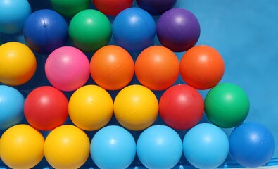 multicolored bright plastic balls on an even background lie on the surface of the water in a summer pool top view