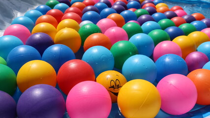 Fototapeta na wymiar multicolored plastic balls without a print filling an inflatable pool and one of them is a rubber ball featuring a funny smiley