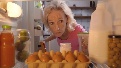 Mature woman looking for ingredients for dinner in fridge