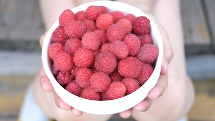 Fresh sweet raspberries in the white ceramic bowl in the kid hands near old wooden surface Organic Raspberry. Healthy breakfast, vegan vegetarian diet. Fresh farm berries