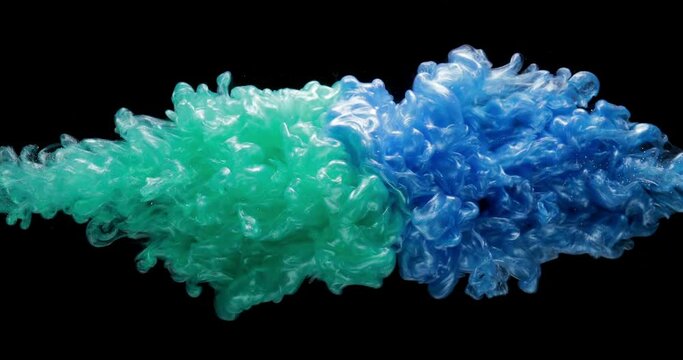 Teal green and light blue fluid pearl inks are exploding and creating gorgeous clouds of mixed colors. Slow motion of colorful paints isolated on black background. Abstract art, creative concept