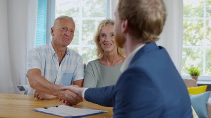 Real estate agent giving handshake to smiling elderly couple after successful agreement
