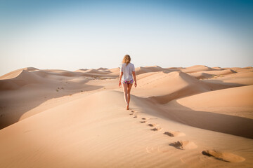 Fototapeta na wymiar Blonde female Caucasian traveler leaving footprints in sand dunes when walking in dessert in Oman.