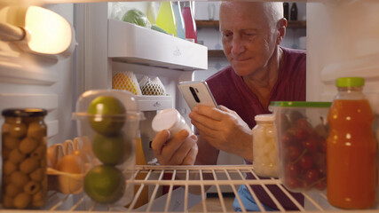 Senior man taking yogurt from fridge for snack checking expiry data