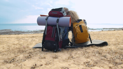 Back view of senior backpack couple sitting on beach enjoying seascape