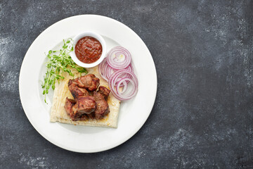 Fried shish kebab with lavash, sauce, microgreen and onion, on a white plate, on a gray background