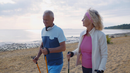 Happy active aged couple trekking along coastline on sandy beach in morning