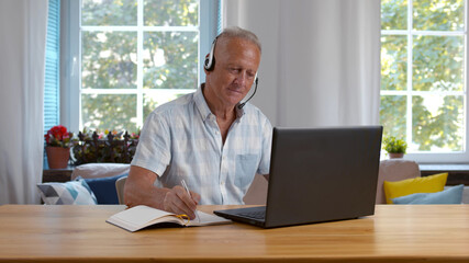 Focused mature businessman wear headphones study online watching webinar