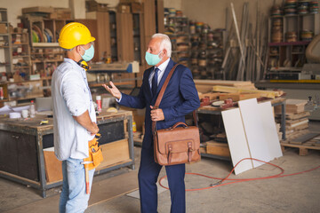 Two caucasian workman standing and talking, wearing face masks