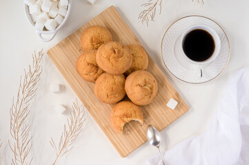 a lot of cheese biscuit cookies on a wooden cutting board, a white cup of coffee and saucers, refined sugar, dry twigs - flat lay