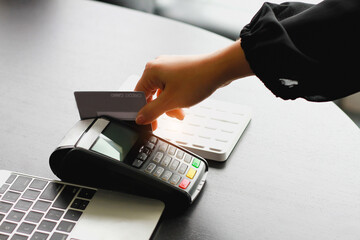 A woman using hand credit card swipe machine for sell products in the shop. Concept of spending via credit card.