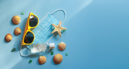 Summer 2020 concept. Travel and protection against coronavirus and other infections. Protective disposable mask, sunglasses, antiseptic, starfish and seashells on blue sunlit background. Banner