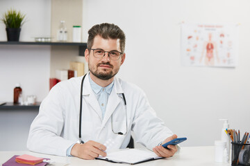 doctor holding smartphone sitting in medical cabinet