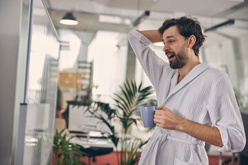 Fototapeta premium Sleepy young man yawning and holding cup of coffee