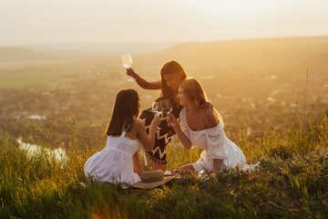 Young beautiful women female friends in tender dresses have summer picnic on a mountain at sunset. Women have a good time together. Girlfriends on a picnic on a warm evening at sunset.