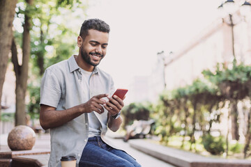 Young handsome student man using smartphone. Smiling joyful guy summer portrait. Handsome man looking at mobile phone - Powered by Adobe