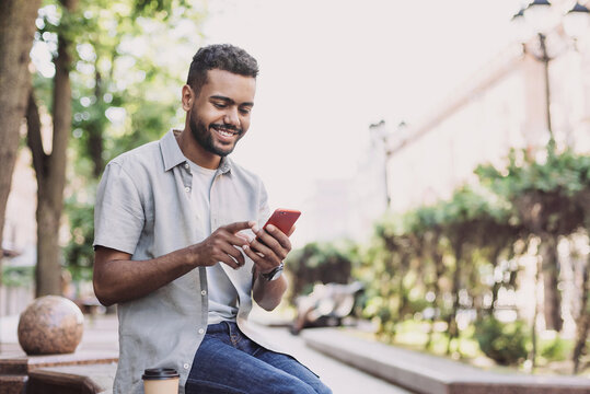 Young handsome student man using smartphone. Smiling joyful guy summer portrait. Handsome man looking at mobile phone