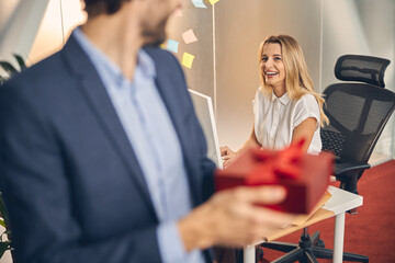 Cheerful young woman looking at male colleague with present
