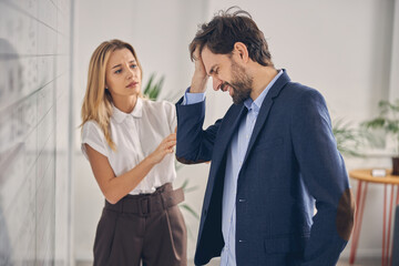 Bearded man having headache while working with lady in office