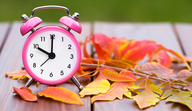 Daylight savings time in autumn fall, retro alarm clock on a wooden background with orange leaves, web banner