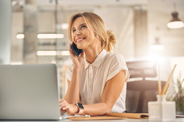 Cheerful young woman having phone conversation at work