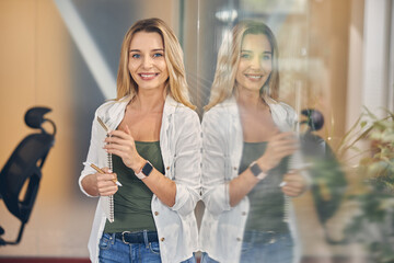 Joyful young woman standing by glass wall in office