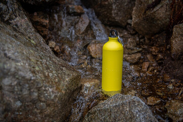 Żółta metalowa butelka na wodę stojąca w górskim potoku
