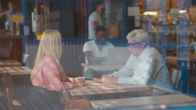 View through window ofn senior couple in love sitting in cafe talking and drinking coffee