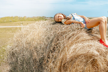 A small child a girl with pigtails lies on a bale of hay in the summer