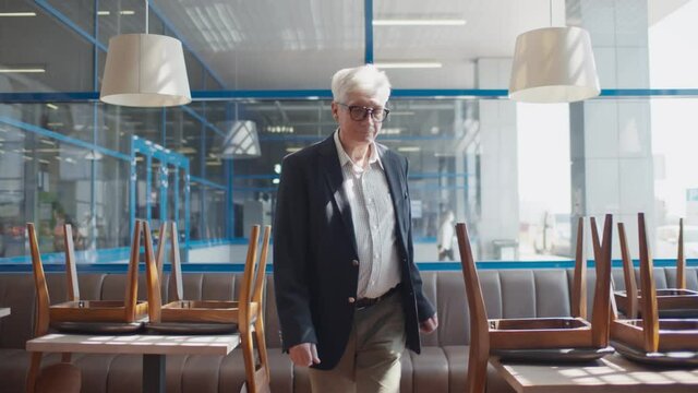 Sad senior small business owner walking in empty cafe closed because of quarantine