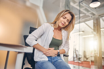 Upset young woman suffering from stomachache in office