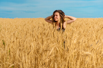 Naklejka na ściany i meble A pretty young woman with long hair stands in a wheat field, a place for text and sun glare