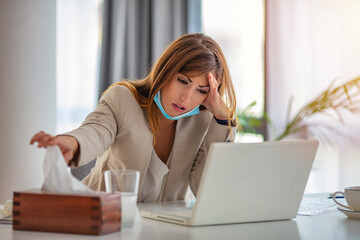 Shot of a frustrated businesswoman using a tissue to sneeze in while being seated in the office. Shot of a young businesswoman blowing her nose while working in an office