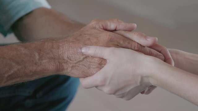 Close up of daughter hands holding father hands. Detail hand of woman consoling old man. Helping hands, care and elderly comfort concept.